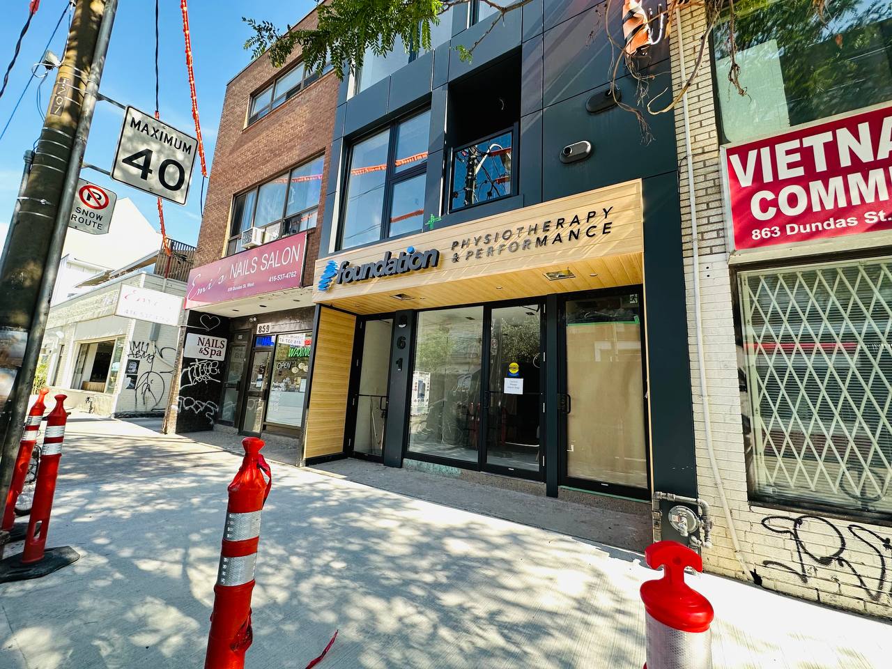 Modern storefront renovation for a clinic on an urban street, contrasting sleek dark grey panels with bright, light oak-finish wood-look aluminum siding accents around the recessed entryway.